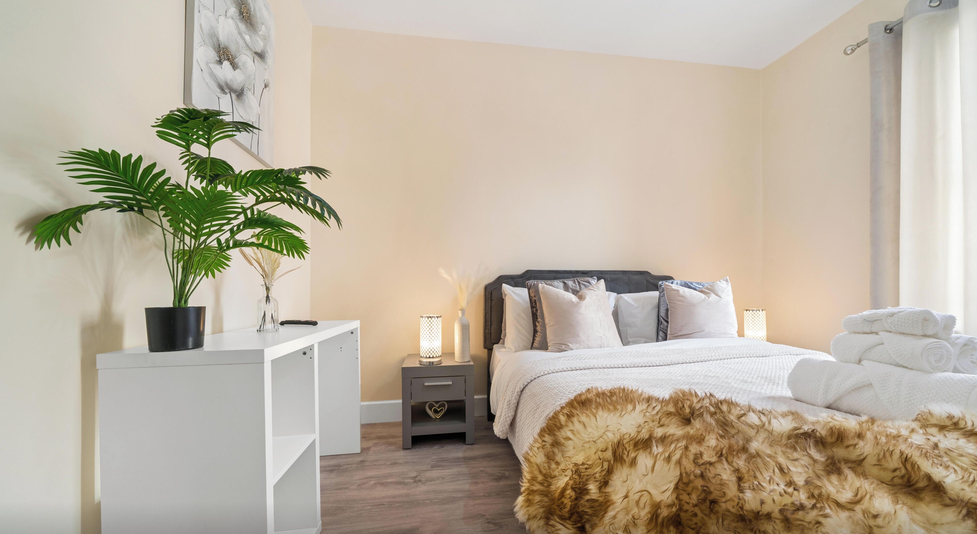 Un dormitorio con cama, mesitas de noche, una planta en maceta y una alfombra mullida.