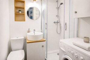 Ein modernes Badezimmer mit Toilette, Waschbecken, Dusche und Waschmaschine.