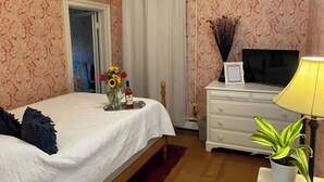 Ett sovrum med en säng, en byrå, en tv och en krukväxt.