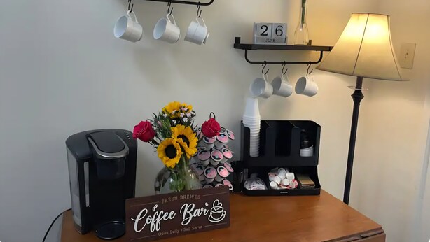 En kaffestation med en skylt, muggar hängda på krokar, en lampa och en datummätare.