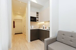 A modern kitchen with a microwave, kettle, and coffee maker, a grey sofa, and a wooden floor. - Bright, stylish studio in center (Riga)
