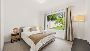 Une chambre à coucher avec un lit, une table de chevet, une lampe et une vue sur la verdure.