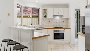 Una cocina compacta con armarios blancos, cocina a gas, horno y un pequeño sector con barra y taburetes.