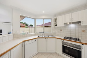 A modern kitchen with white cabinets, a dishwasher, a sink, a stove, and an oven. - 3 Bed Home Near Crown, City, Optus Stadium & Airport (Carlisle)