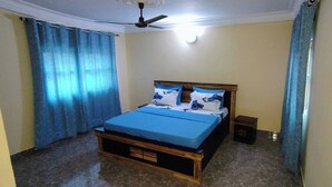 Ein Schlafzimmer mit einem Bett, Vorhängen, einem Deckenventilator und einem kleinen Nachttisch.