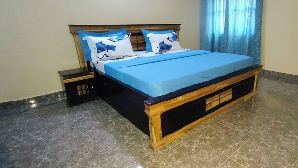 Ein Bett mit blauer Bettdecke und passenden Kissen, ein Holz-Kopfteil, ein Nachttisch mit Schublade und ein Marmorboden.
