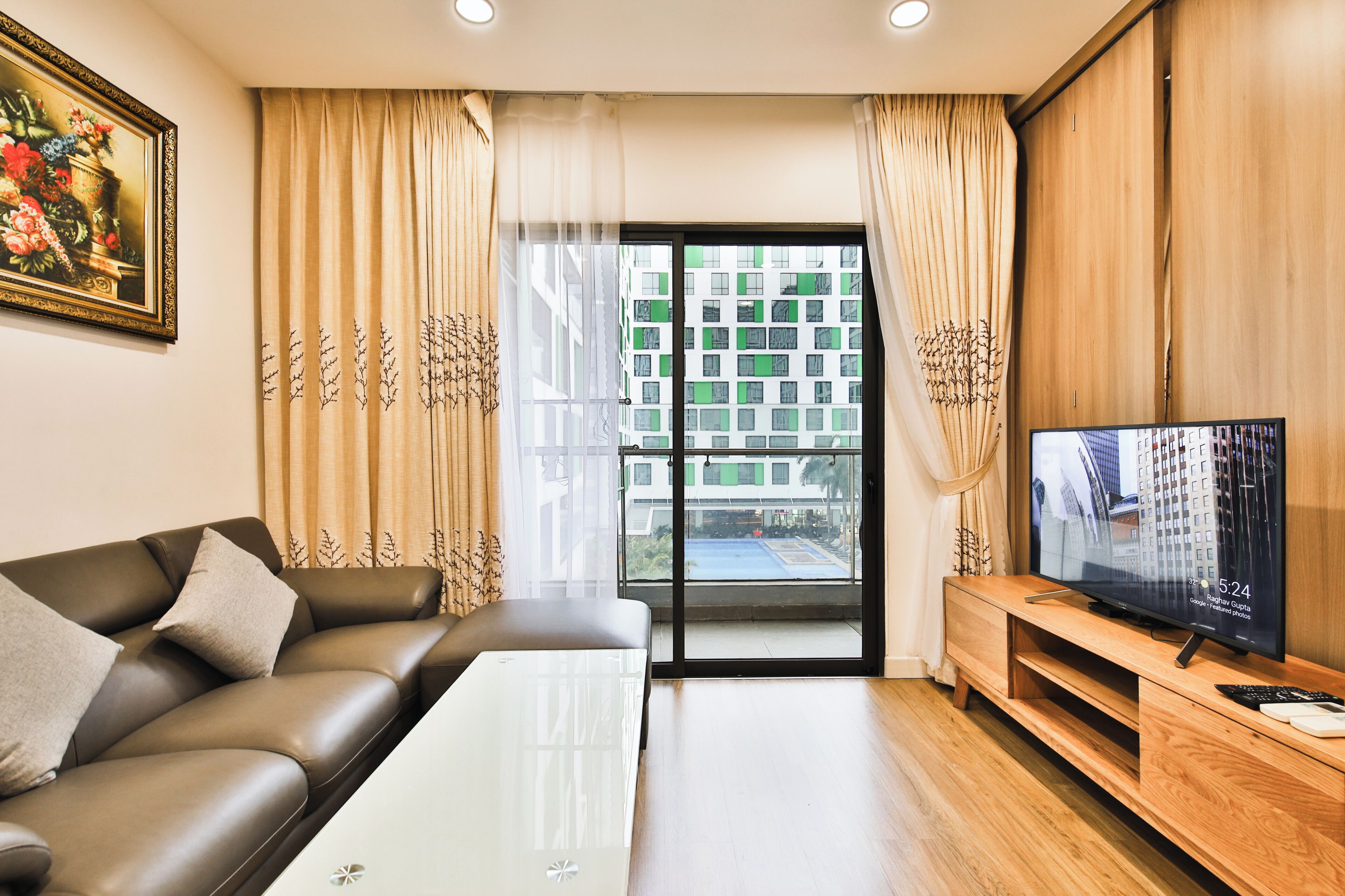 Un salon moderne avec un canapé, une table basse, un téléviseur et un balcon offrant une vue sur les immeubles.