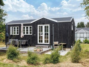 A black wooden building with a large window and a door, outdoor seating, and a small table. - 2 Person Holiday Home in Dannemare (Dannemare)