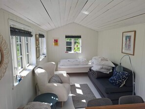 Ein gemütliches Zimmer mit einem Bett, einem Sofa, einem Sessel, einem kleinen Tisch und einem Fenster mit Jalousien.