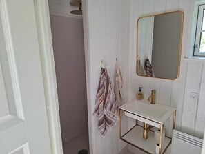 Ein Badezimmer mit Dusche, einem weißen Waschbecken mit Goldarmatur und einem Spiegel mit goldener Rahmung.