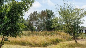 A natural landscape with trees, grass, and a building in the background. - 2 Person Holiday Home in Dannemare (Dannemare)