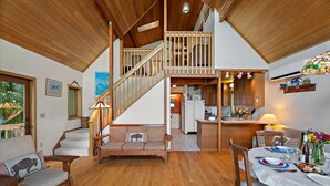 Ein geräumiger Wohnbereich mit einer Holztreppe, einem gedeckten Esstisch und einer Küche im Hintergrund.