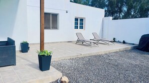 A patio area with two lounge chairs, a potted plant, and a gravel path.
