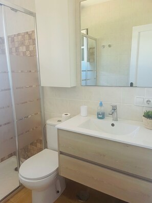 A bathroom with a shower, toilet, sink, and mirror.