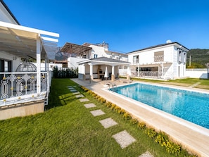 A modern villa with a swimming pool, a covered patio, and a well-maintained lawn.