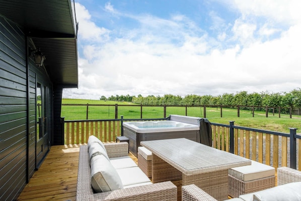A wooden deck with outdoor furniture, a hot tub, and a view of a vineyard.