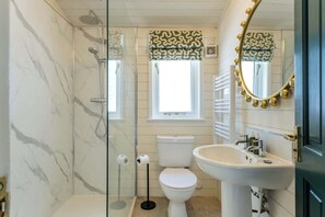 A bathroom with a glass-enclosed shower, a toilet, a sink, and a mirror with gold accents. - The Paddock Lodge with Hot Tub (Leicestershire)