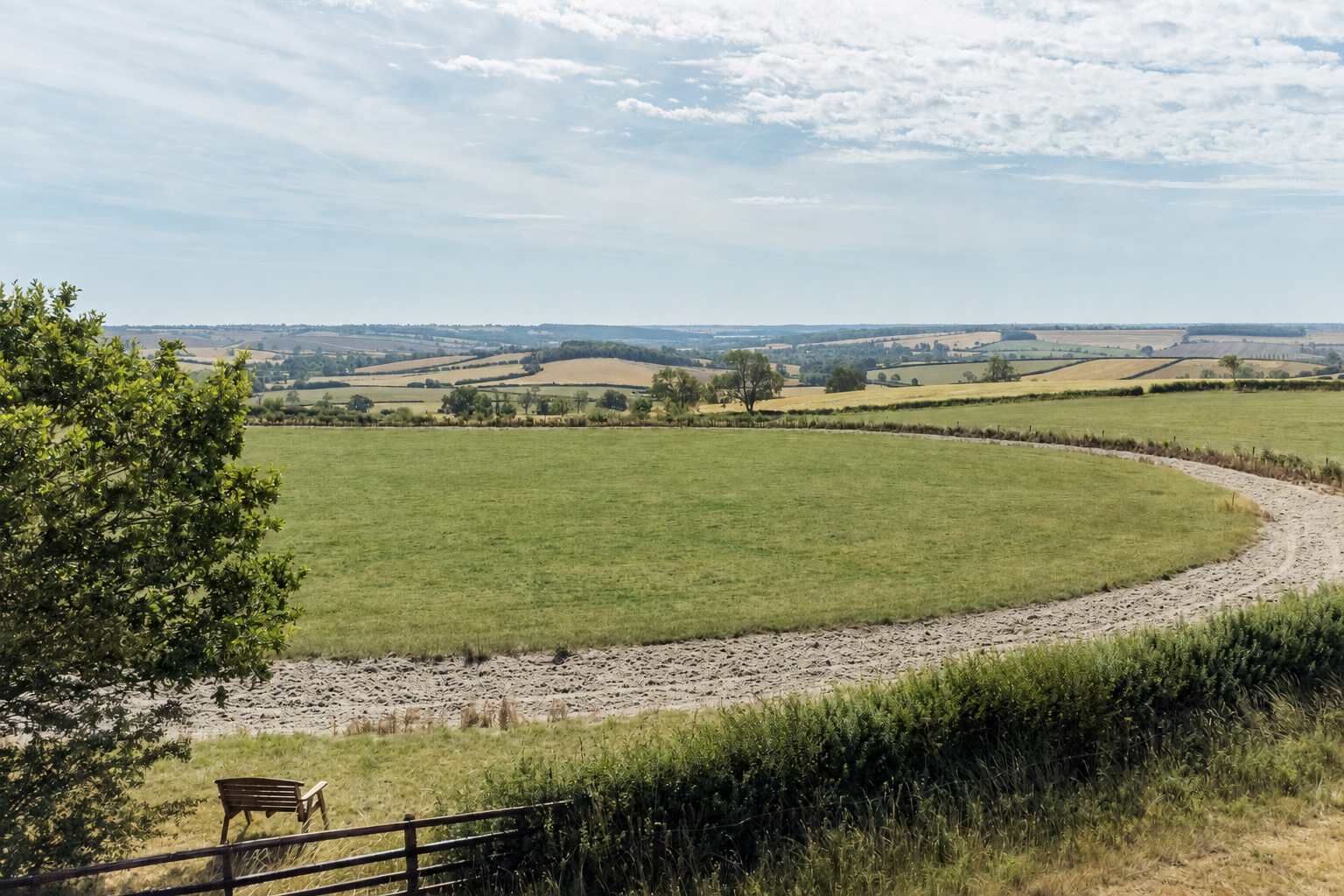Un paysage rural avec un chemin de terre sinueux, un banc et un arbre.