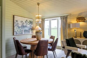 A dining area with a round wooden table, leather chairs, a vase, and a painting on the wall. - The Paddock Lodge with Hot Tub (Leicestershire)