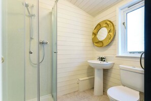 A bathroom with a glass shower enclosure, a pedestal sink, a toilet, and a window with a view.
