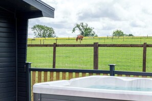A wooden deck with a hot tub, a fenced pasture with a horse, and a cloudy sky. - The Paddock Lodge with Hot Tub (Leicestershire)