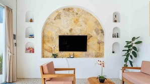 Una sala de estar con pared de arco de piedra, un televisor de pantalla plana, muebles de madera y plantas en macetas.