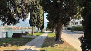 A riverside walkway with benches, trees, and a view of a cityscape. - Second Lake House - Affitti Brevi Italia (Malgrate)