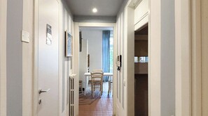 A narrow hallway with white walls, a door on the left, and a window with blue curtains in the background. - Second Lake House - Affitti Brevi Italia (Malgrate)