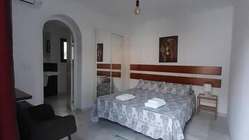 A bedroom with a bed, a chair, a bedside table, and a door leading to another room.