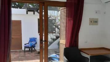Una habitación con cama, escritorio, silla y puerta corrediza de vidrio que da a un espacio exterior con una silla y una mesa.