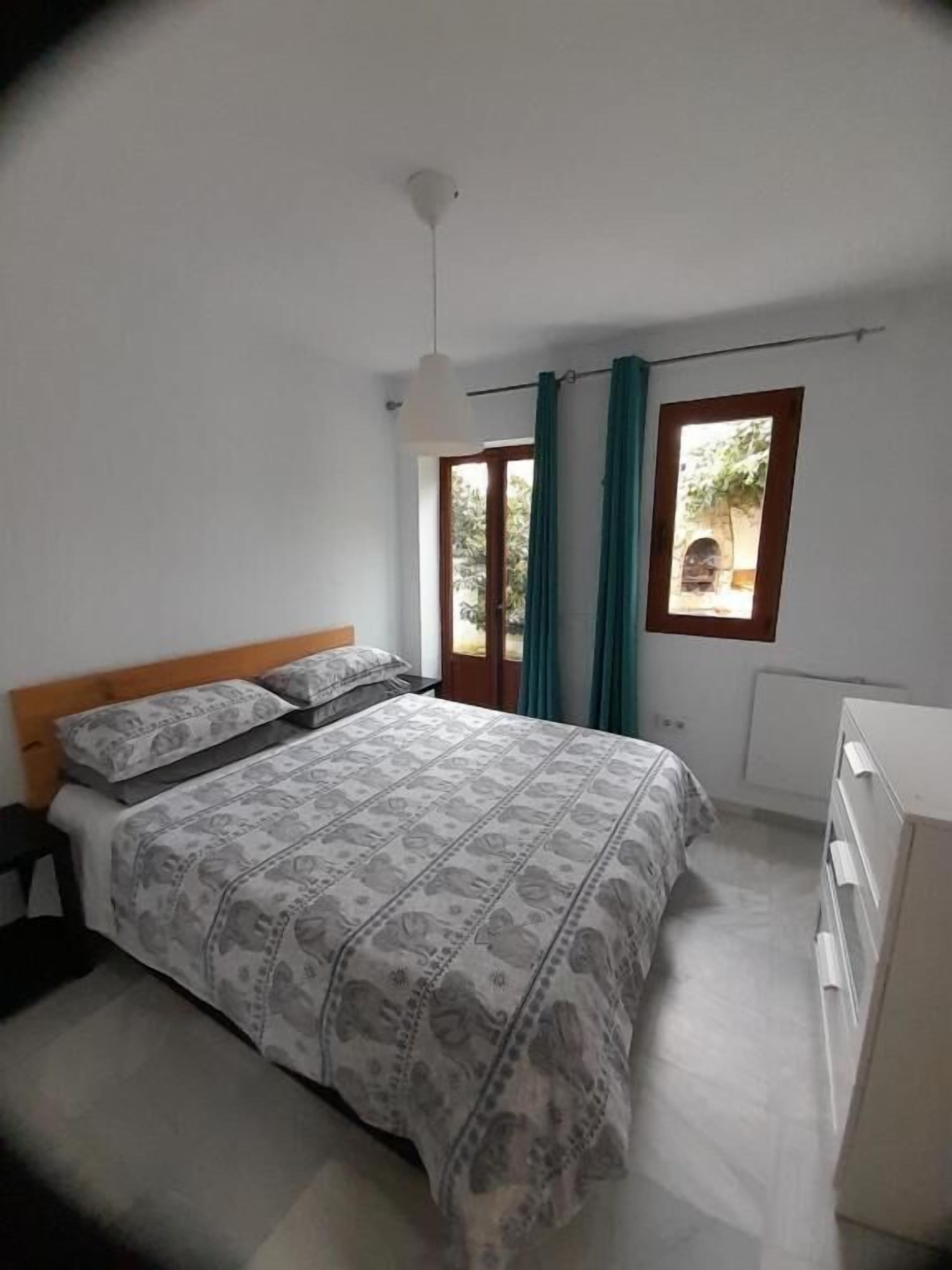 A bedroom with a bed, a nightstand, a dresser, a window with curtains, and a ceiling light.