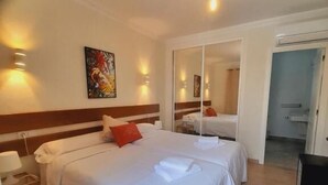 Habitación de hotel con dos camas, un espejo, un cuadro y una puerta que da a un baño.