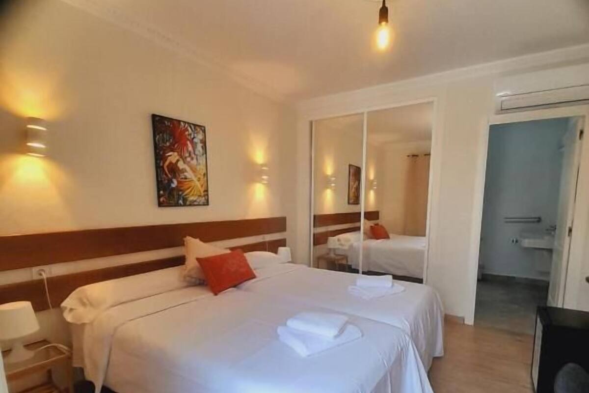 A hotel room with two beds, a mirror, a painting, and a door leading to a bathroom.