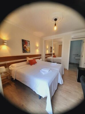 Una habitació d'hotel amb dos llits, un mirall, un quadre i una porta que dona a un bany.