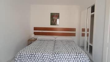 Un dormitorio con cama, cabecera, mesita de noche, luz empotrada en la pared y ventana.