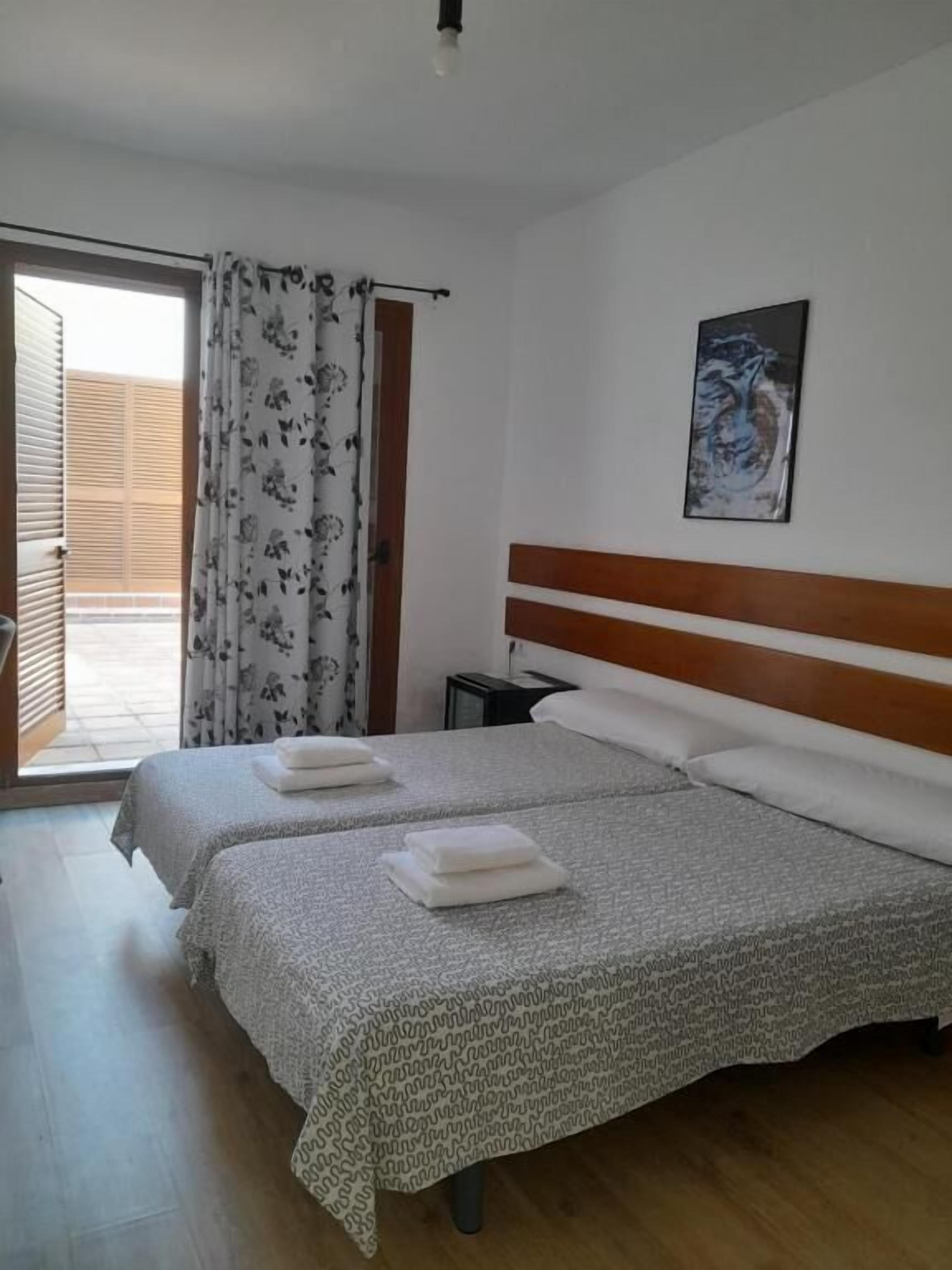 Habitació d'hotel amb dos llits, un capçal de llit de fusta, un quadre a la paret i una finestra amb cortina.