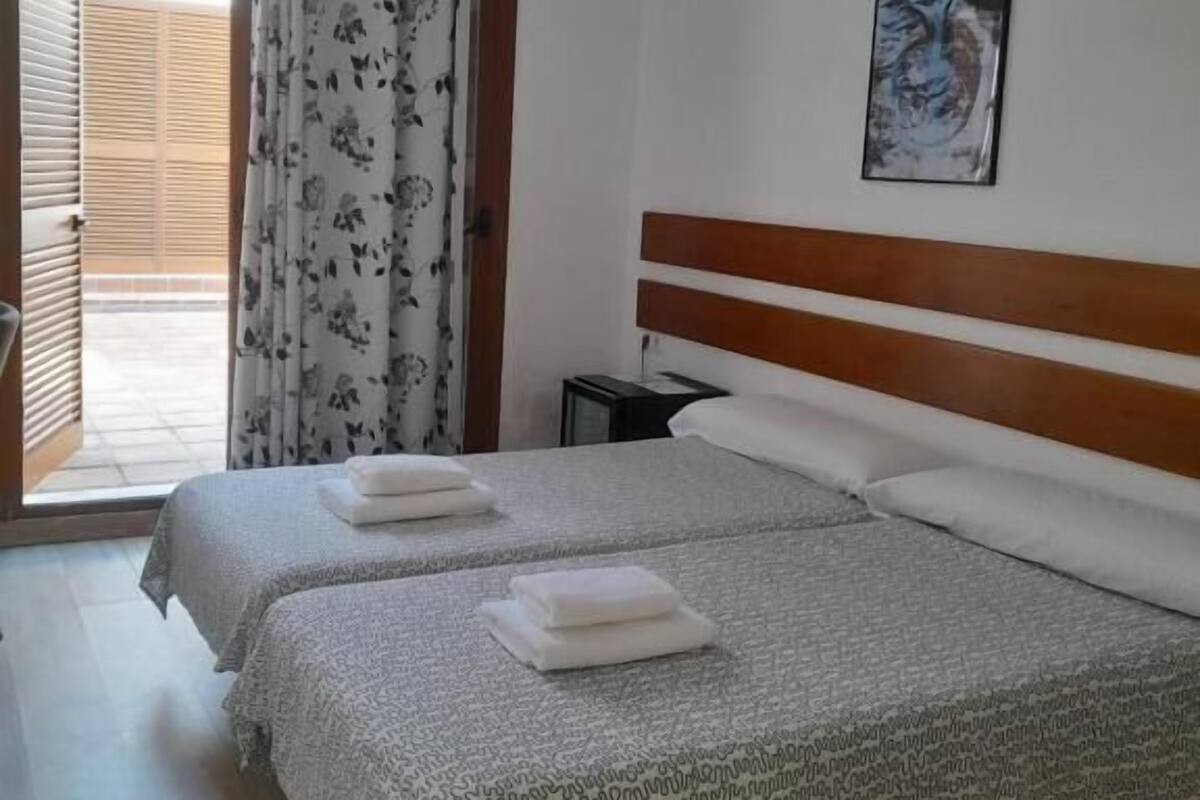 A hotel room with two beds, a wooden headboard, a painting on the wall, and a window with a curtain.