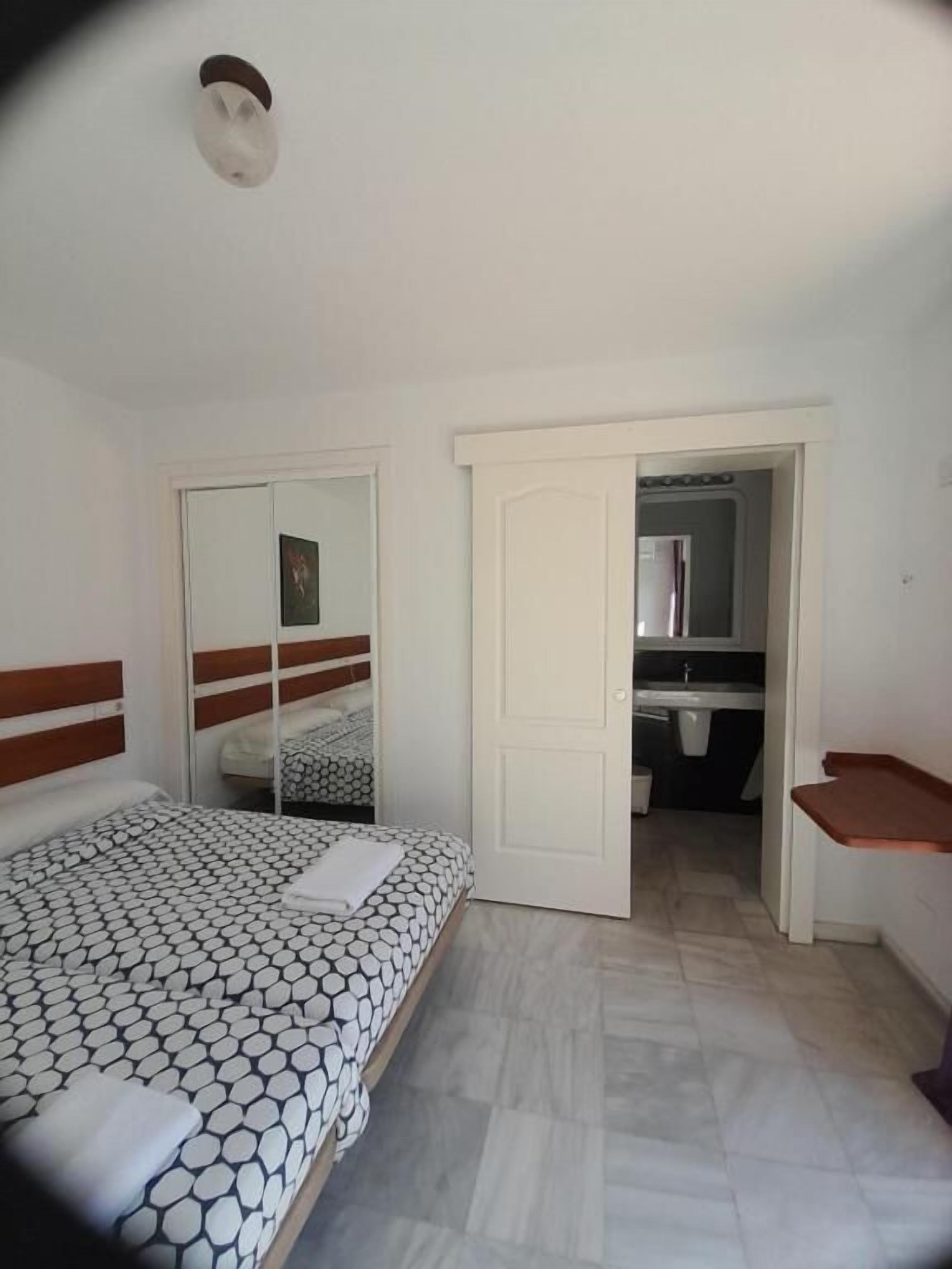 Une chambre à coucher avec un lit, un miroir, une armoire et une salle de bain visible à travers une porte ouverte.