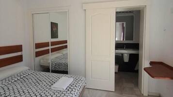 Une chambre à coucher avec un lit, un miroir, une armoire et une salle de bain visible à travers une porte ouverte.