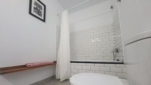 Un baño con inodoro blanco, ducha con cortina blanca y pared con azulejos.