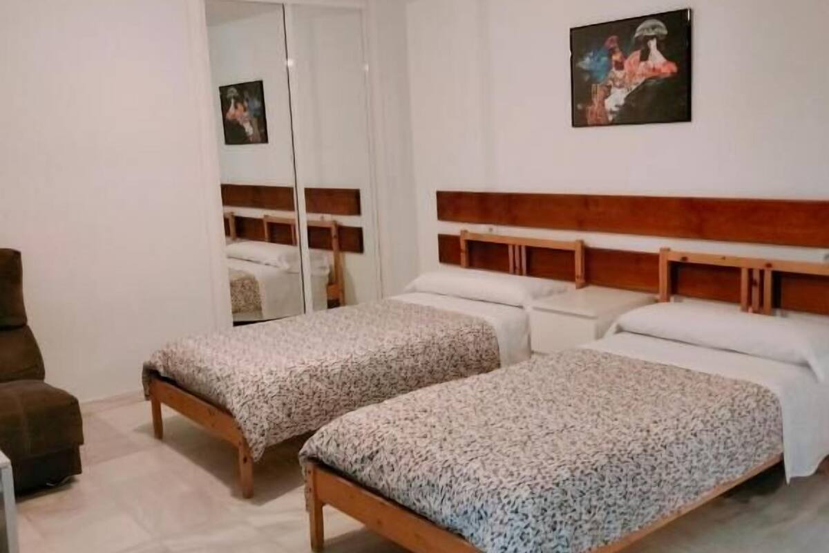 A bedroom with two beds, a wardrobe, a chair, and a painting on the wall.