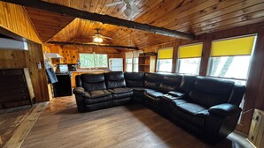 A wooden cabin interior with a large L-shaped leather sofa, a ceiling fan, and a kitchen area. - Lakefront Retreat on Sebasticook Lake (Newport)