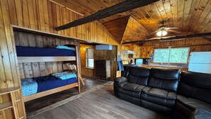 A cabin interior with a bunk bed, a leather sofa, a kitchen area, and a window with a view of trees. - Lakefront Retreat on Sebasticook Lake (Newport)