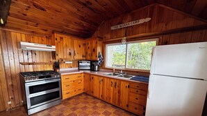 A cabin kitchen with wooden cabinets, a stove, oven, sink, and a refrigerator. - Lakefront Retreat on Sebasticook Lake (Newport)