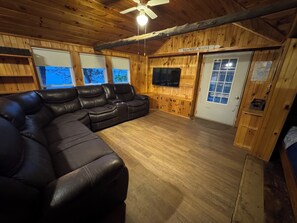 A wooden interior with a sectional sofa, a ceiling fan, and a TV mounted on the wall.