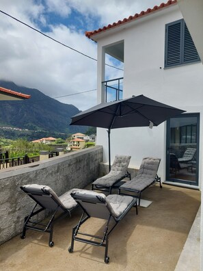 Ein Balkon mit Liegestühlen und einem großen Sonnenschirm, mit Blick auf eine gebirgige Landschaft.