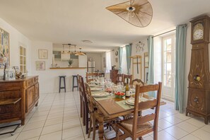 A dining area with a wooden table set for a meal, chairs, a clock, and a kitchen in the background. - Le Clos Vinzelles - House + outbuilding in the heart of the vineyards, large garden (Vinzelles)