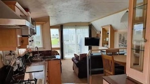 A compact kitchen with a gas stove, a dining area with a table and chairs, and a television mounted on the wall. - 2 Bed - Sleeps 6 - Lake View - Beach Access - Pets (Skegness)