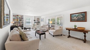 Een woonkamer met een bank, fauteuils, een salontafel, een boekenkast en een schilderij aan de muur.