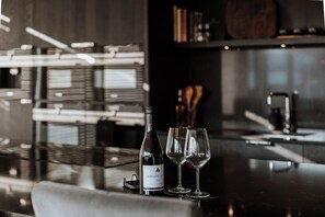A bar area with a bottle of Domaine Laroche wine, two glasses, and a modern kitchen in the background. - Luxury two Story Penthouse With Roof top Terrace (Shrewsbury)